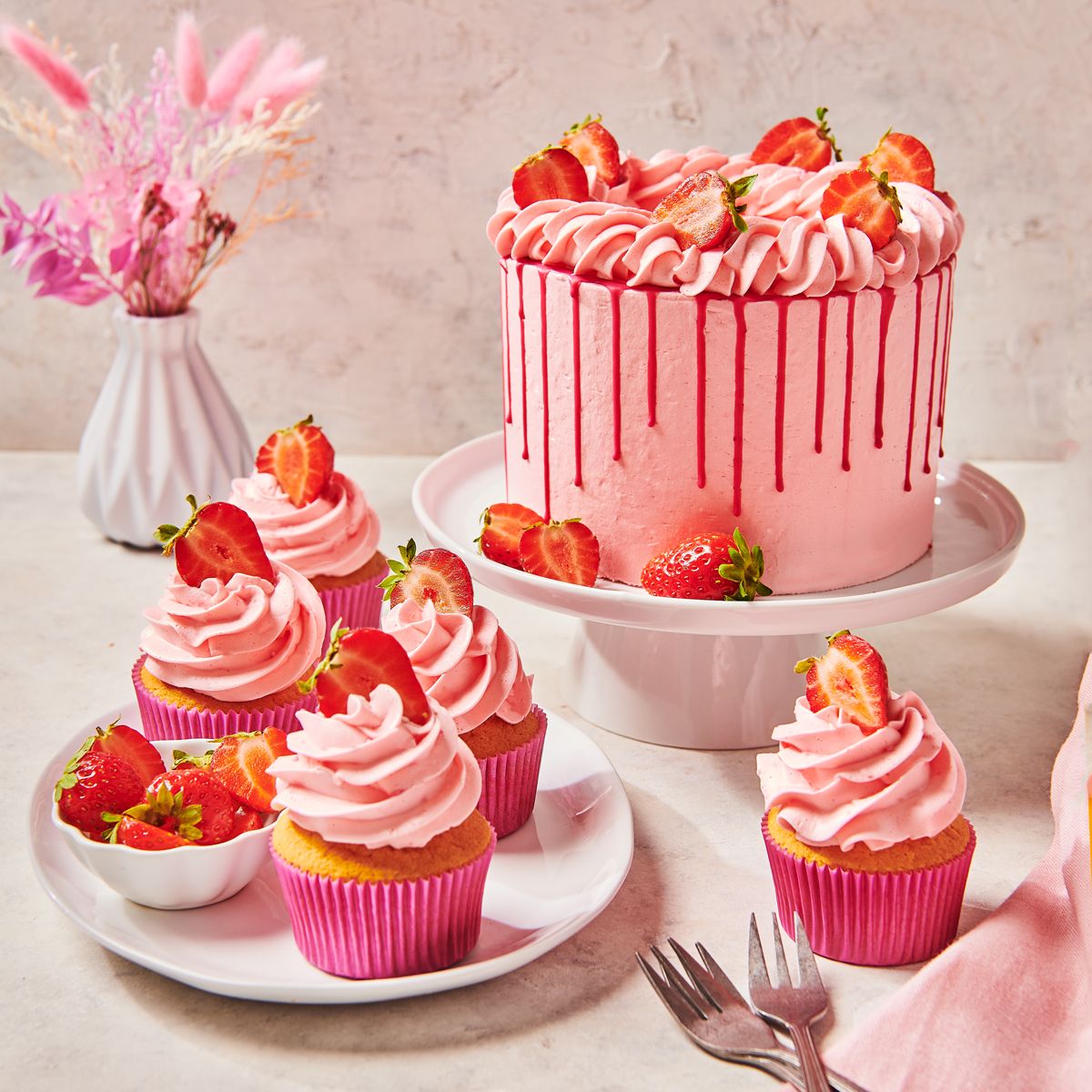 FunCakes Erdbeertorte Enchanted Cream und CupCakes auf einem Teller mit Vase im Hintergrund
