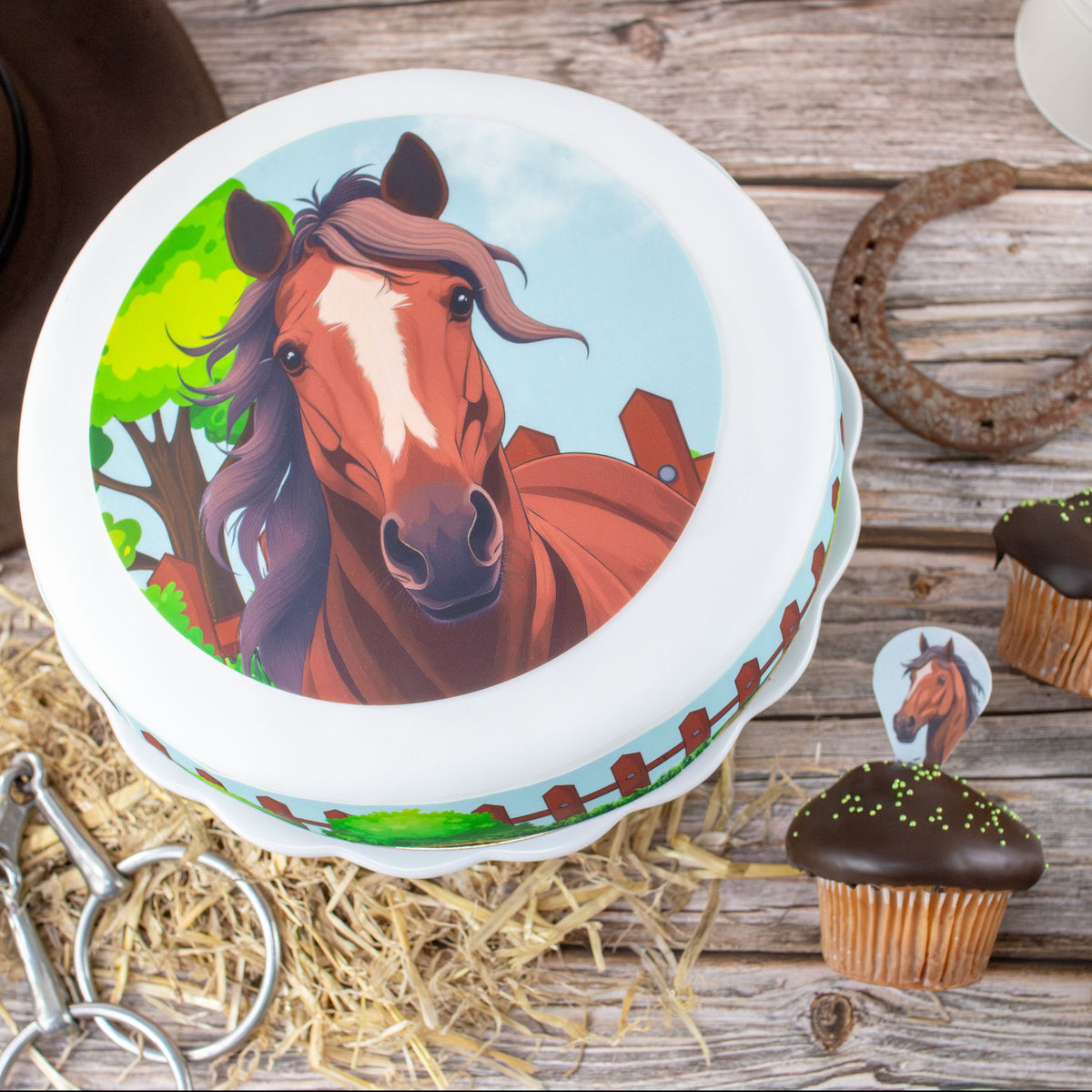 Torte mit Tortenbild Pferdekopf auf Holztisch mit Stroh und Muffins