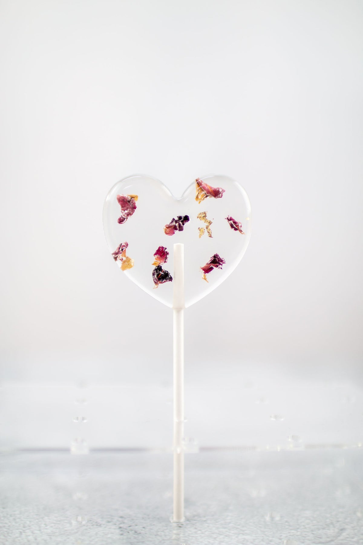 herzförmiger Blütenlolli mit roten Rosenblättern in Halter